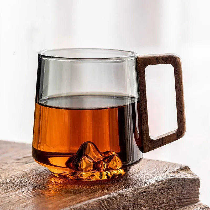 Handcrafted glass coffee mug featuring a stunning mountain design base and comfortable wooden handle. Great home decor.