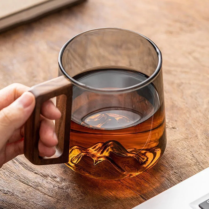 Elegant tea cup made from borosilicate glass, showcasing a detailed mountain base and a stylish wooden handle. Unique drinkware.
