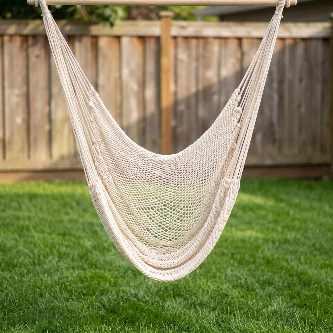 Empty white boho tasseled hammock ready for tranquil outdoor relaxation, suspended between trees in a sunny yard.
