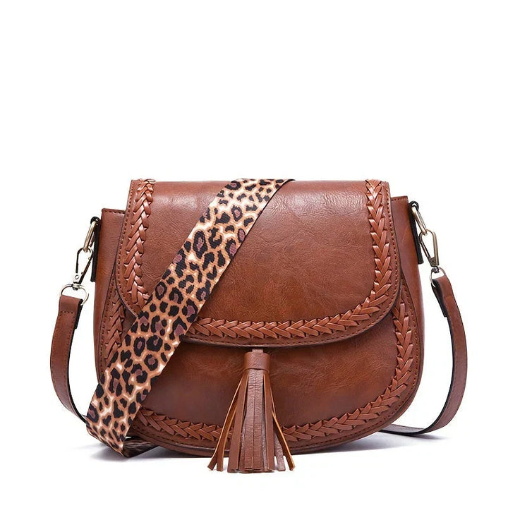 Modern women's saddle bag featuring a long adjustable strap, chic tassels, and a structured design.