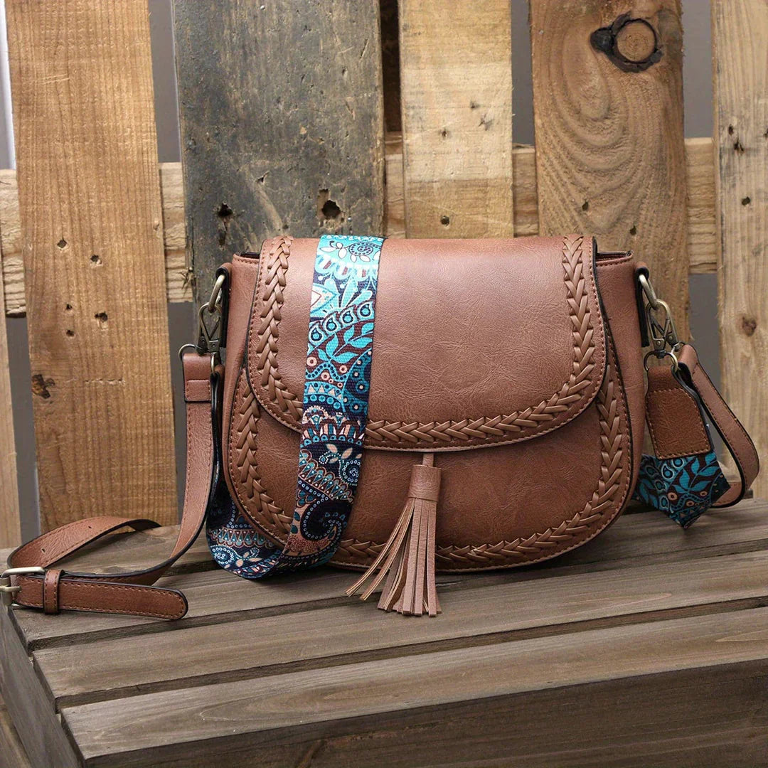 Elegant leather-look women's saddle bag featuring stylish fringe tassels and an adjustable strap.