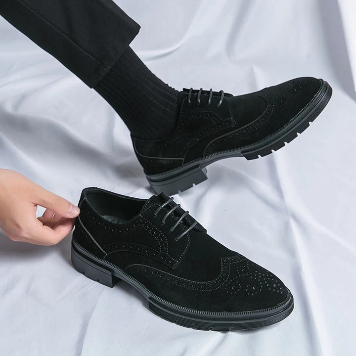 Close-up of men's black suede brogue shoe, highlighting the intricate wingtip detailing and quality material.