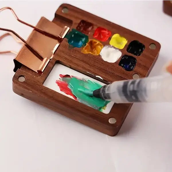 Hand holding a small, portable watercolour painting kit, emphasizing its convenient travel size.