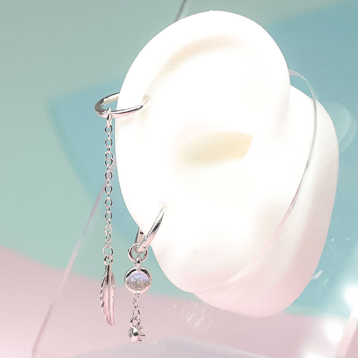 Close-up: Elegant asymmetric feather moonstone sterling silver earrings. Unique women's drop design.