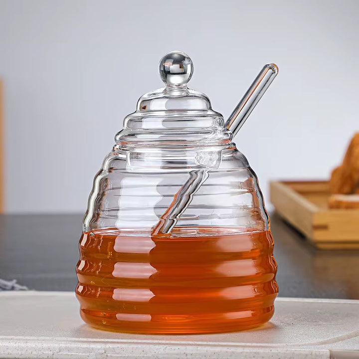 Charming beehive shaped glass honey jar with dipper, excellent for syrup or honey display.