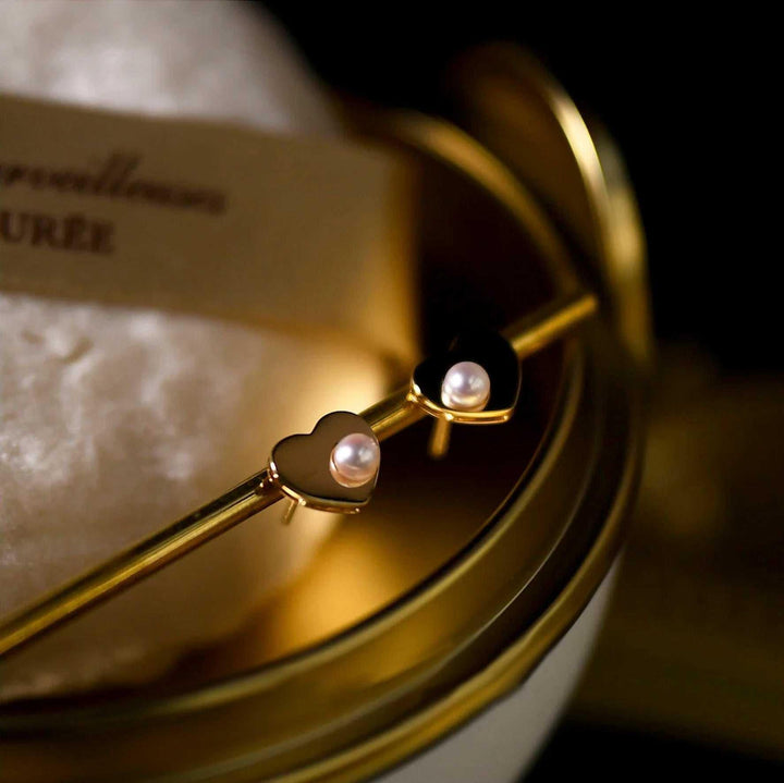 Close-up of elegant women's pearl and gold heart stud earrings, ideal accessory