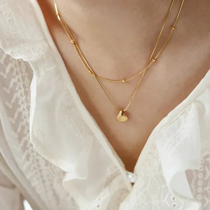 Elegant women's necklace featuring a golden scallop shell and a soft lilac flower pendant, gold plated.