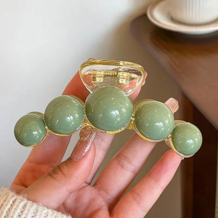 Close-up of a women's elegant green pearl hair clip with gold details, ideal for chic hair fashion.
