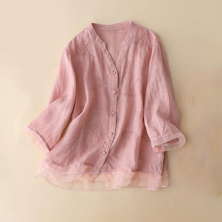 Elegant pink women's v-neck blouse with intricate embroidery and a contemporary layered hem, perfect for sophisticated style.