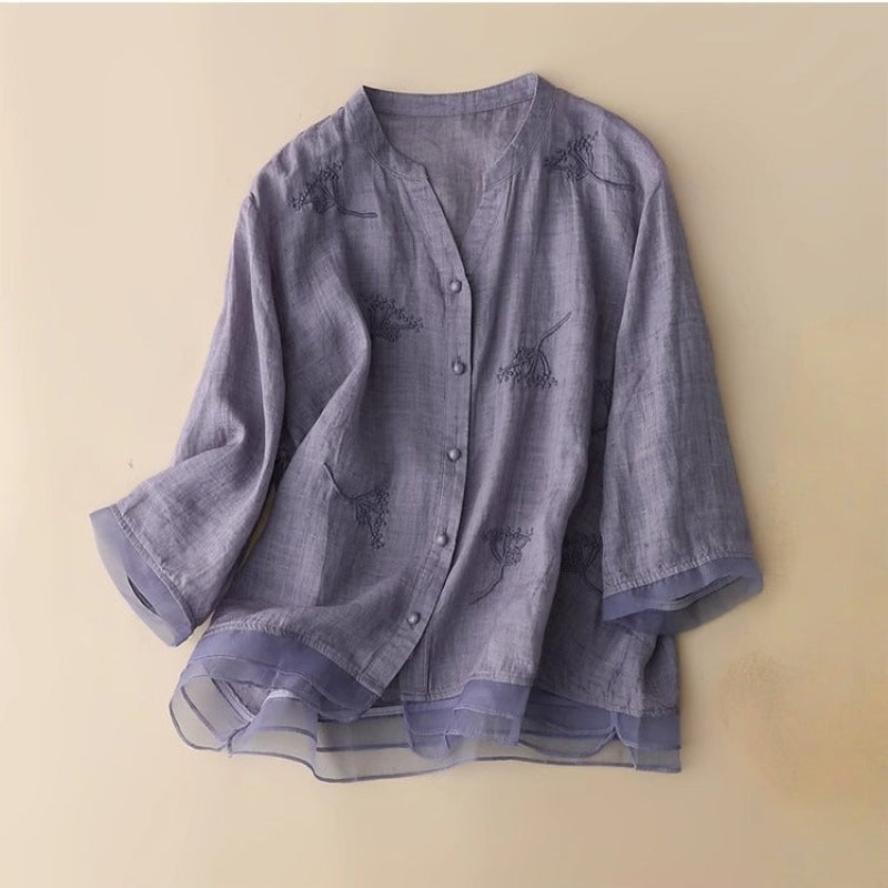 White women's embroidered v-neck blouse, showcasing elegant design and a stylish layered hem. Contemporary fashion.