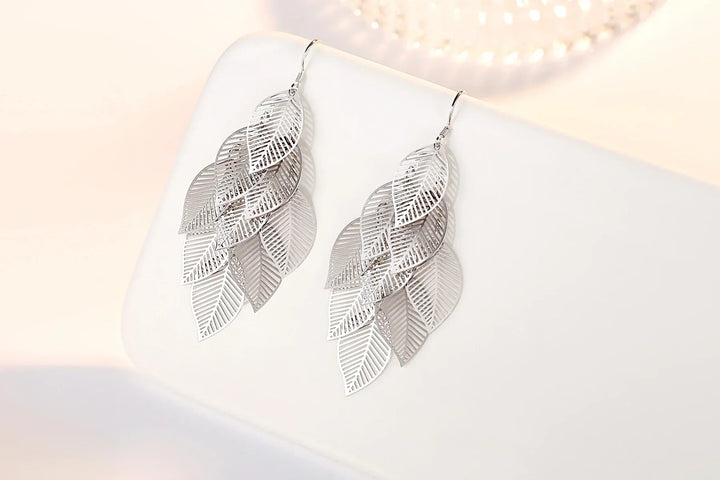 Close-up of delicate layered leaf earrings, sterling silver dangle style. Elegant nature-inspired design.