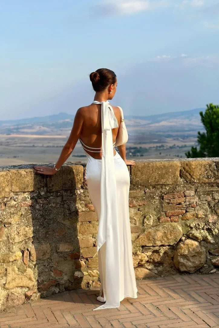 Fitted white maxi dress with a halter neckline & elegant backless design, suitable for formal wear.