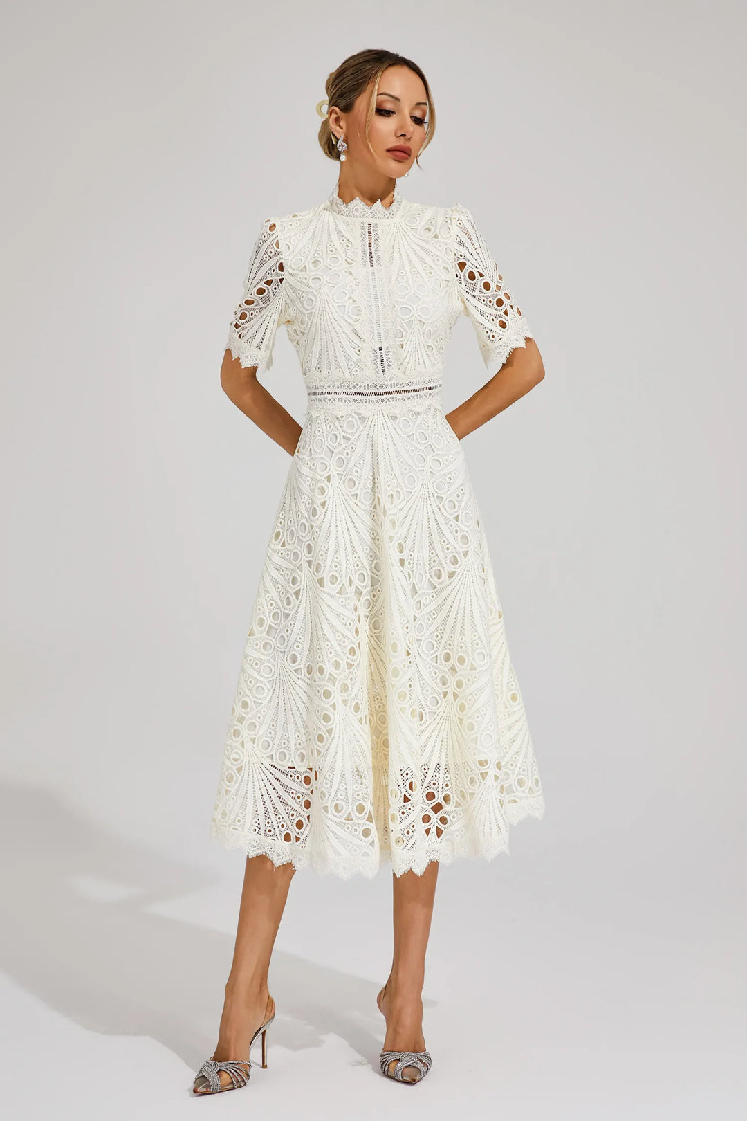 Woman posing gracefully in an elegant white lace midi dress for special occasions.