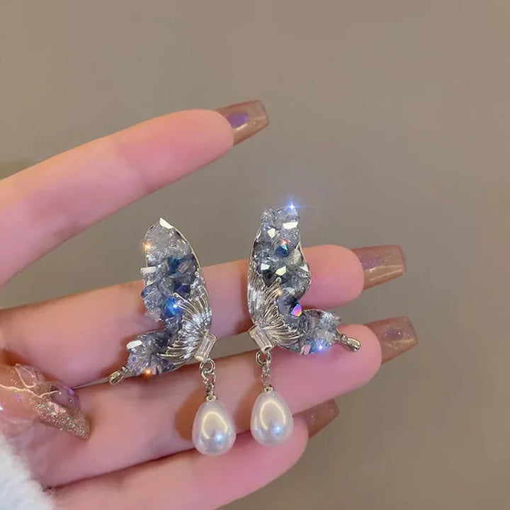 Beautiful women's crystal butterfly wing drop earrings featuring blue crystals and a pearl. Elegant fashion jewelry.