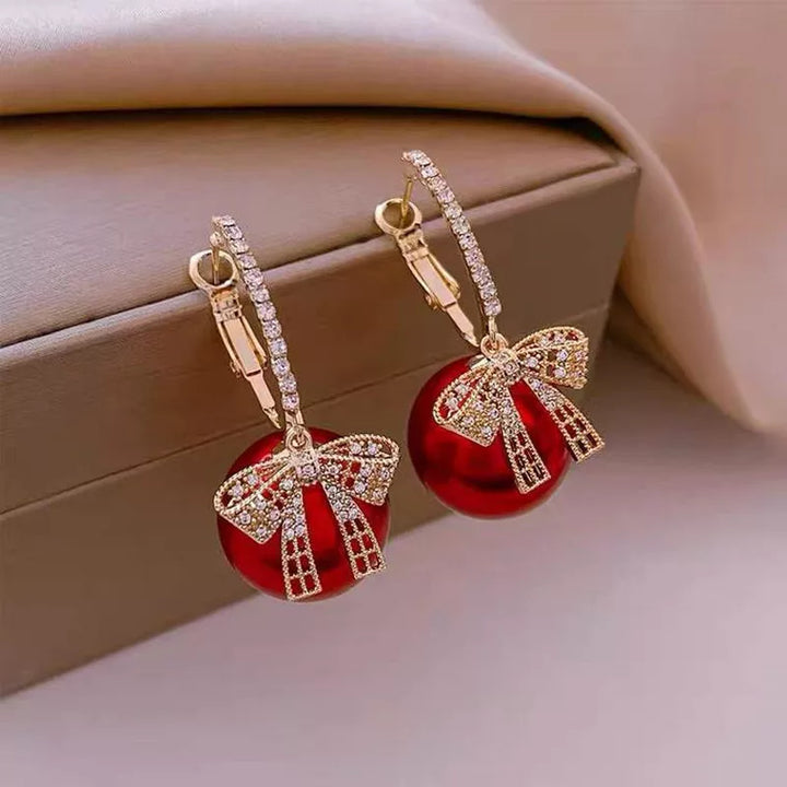 Close-up of women's Christmas pearl drop earrings, featuring delicate red bows & shiny white pearls.