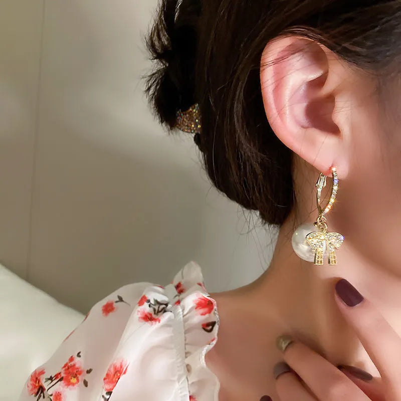 Women's elegant holiday earrings: classic white pearls paired with charming red Christmas bows.