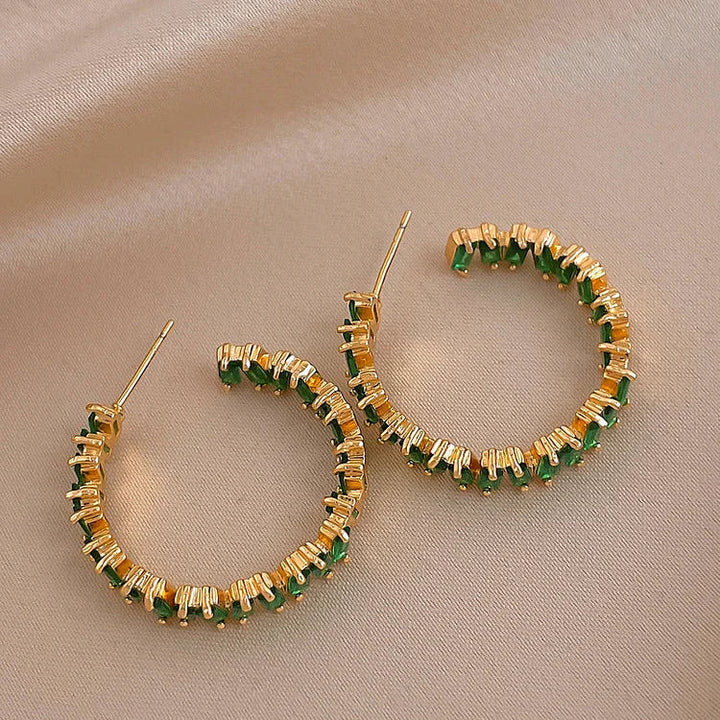 Women's gold-plated hoop earrings with vibrant emerald green crystals, elegant and luxurious jewelry.