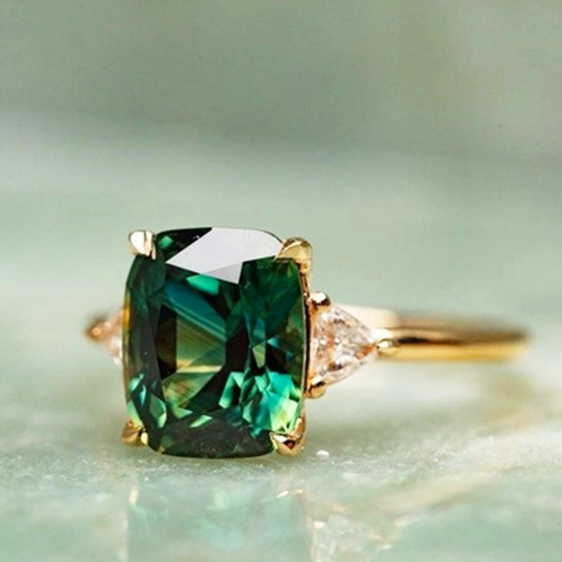 Close-up of a gold plated women's square emerald ring. Luxurious gemstone fine jewelry with a modern design.