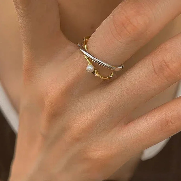 Close-up of a women's sterling silver ring, showcasing its delicate crossed design and single lustrous pearl.