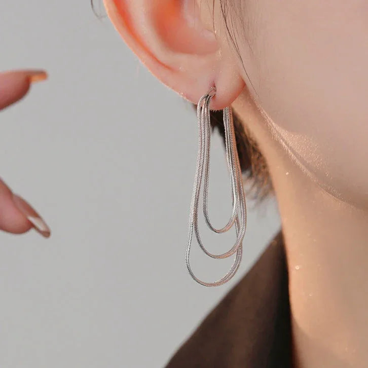 Close-up of chic three-layer chain drop earrings, showcasing intricate layered design in gold or silver.