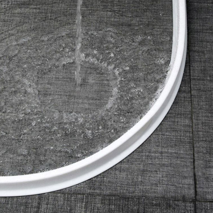 Close-up of a white flexible silicone shower water barrier installed on a bathroom floor.