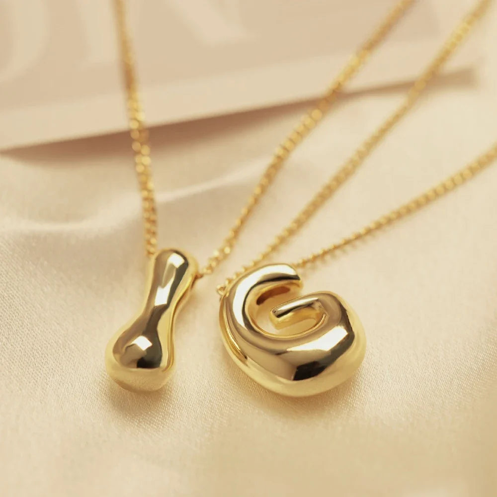 Close-up of a shimmering gold initial letter pendant on a delicate stainless steel chain necklace.