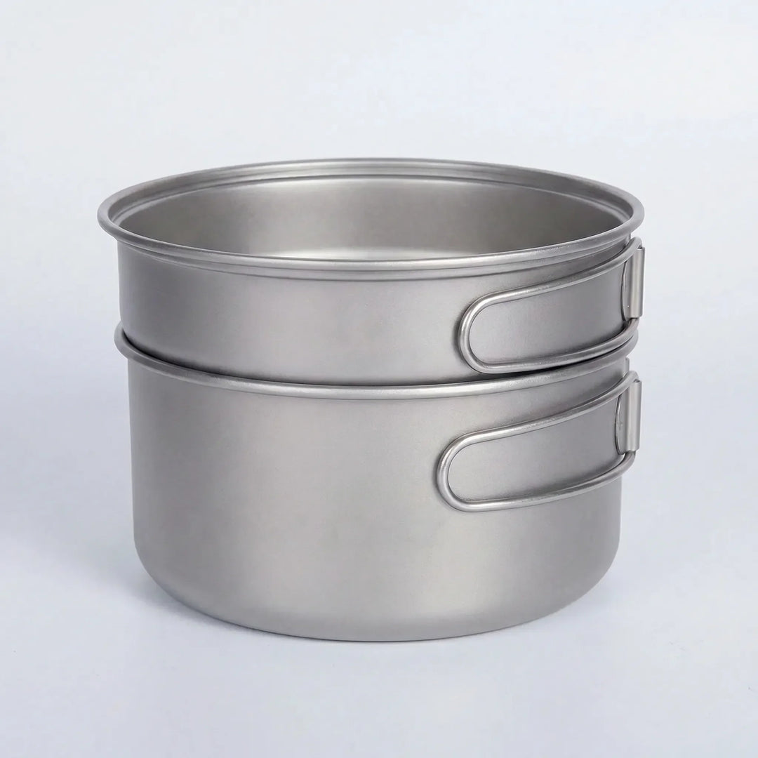 Compact titanium camping pot and pan set with folding handles for easy packing and lightweight outdoor cooking.