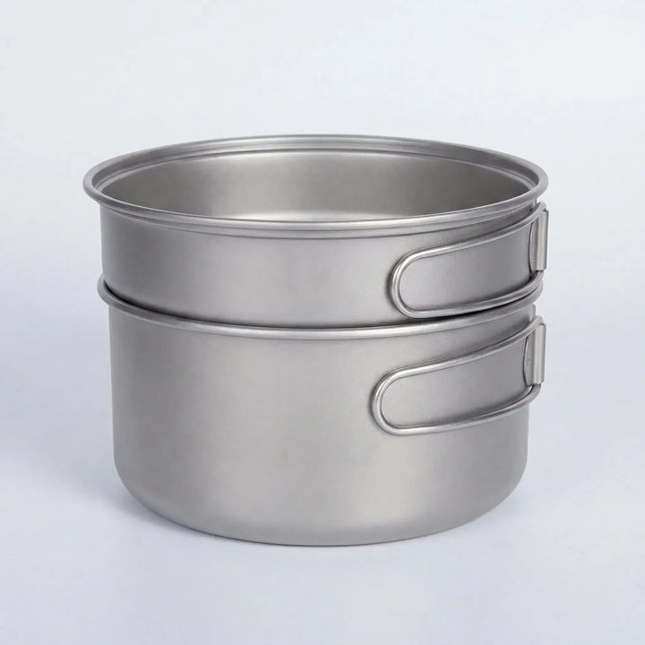 Compact titanium camping pot and pan set with folding handles for easy packing and lightweight outdoor cooking.