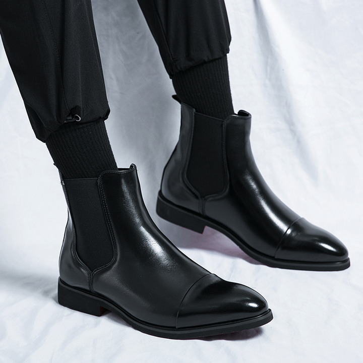 Close-up of a men's brown leather Chelsea boot, highlighting the sleek silhouette and vibrant red sole.
