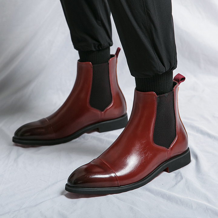 Full shot of men's sharp black Chelsea boots, showcasing the clean lines and unique red sole detail.