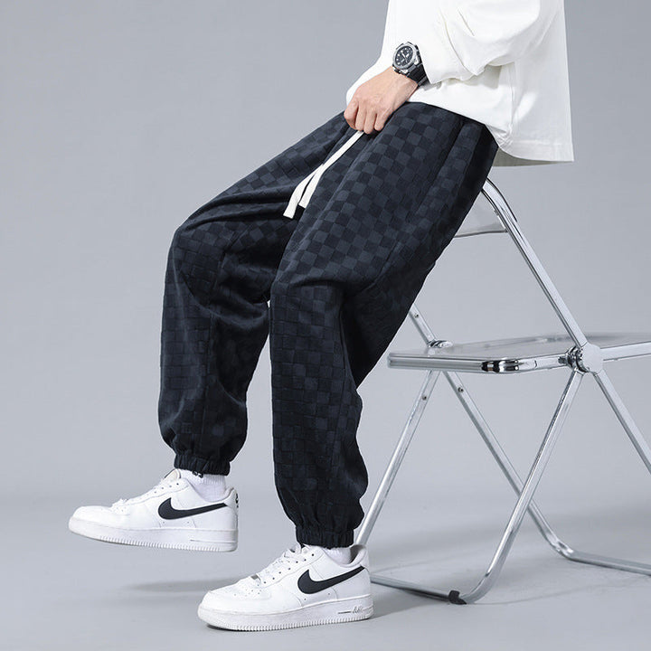 Close-up of black and gray checkerboard men's sweatpants fabric, highlighting pattern and texture.