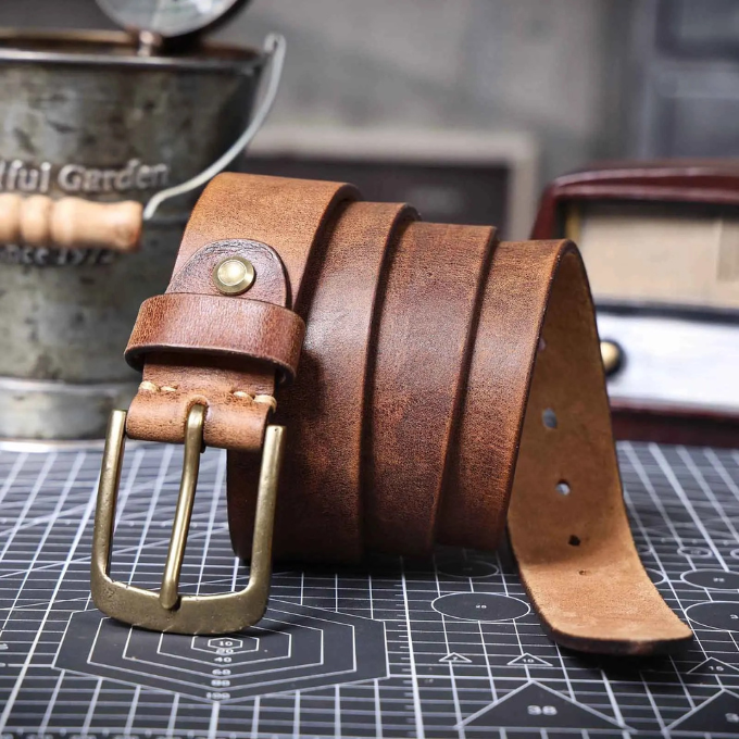 Detail shot of the lustrous polished metal buckle on a classic men's brown leather belt.