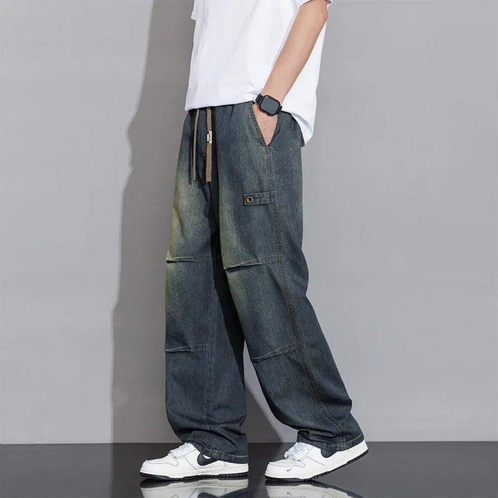 Model wearing men's relaxed fit wide-leg washed jeans with drawstring. Casual, comfortable men's fashion.