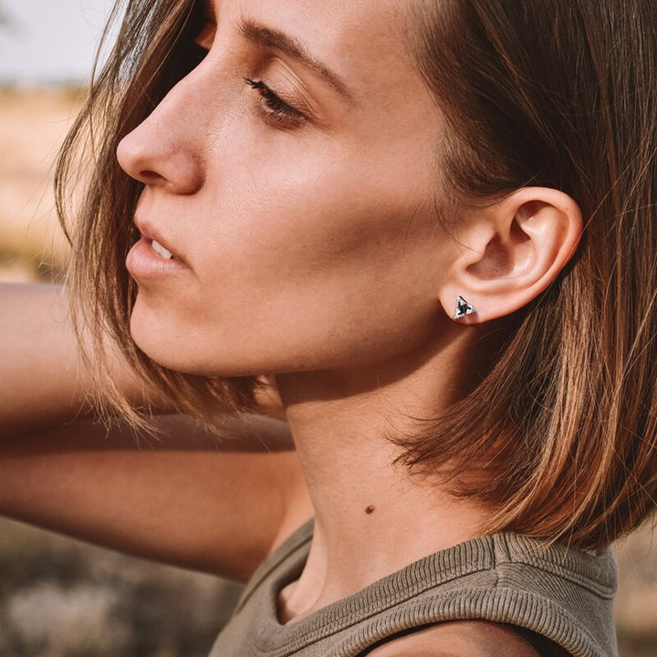 Close-up of a minimalist sterling silver triangle stud earring, showcasing its sleek unisex design and finish.