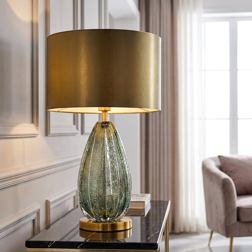 Modern glass base table lamp with green translucent body and white fabric shade illuminating a living room.