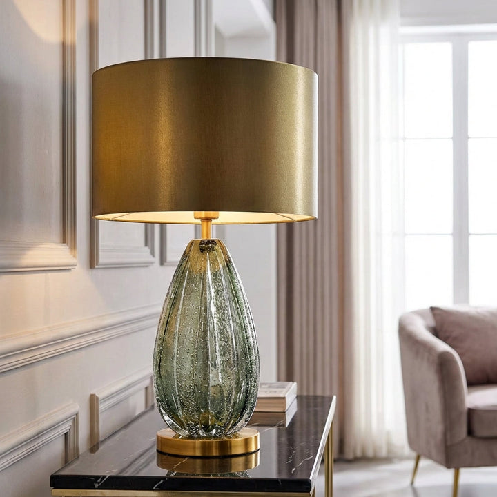 Modern glass base table lamp with green translucent body and white fabric shade illuminating a living room.