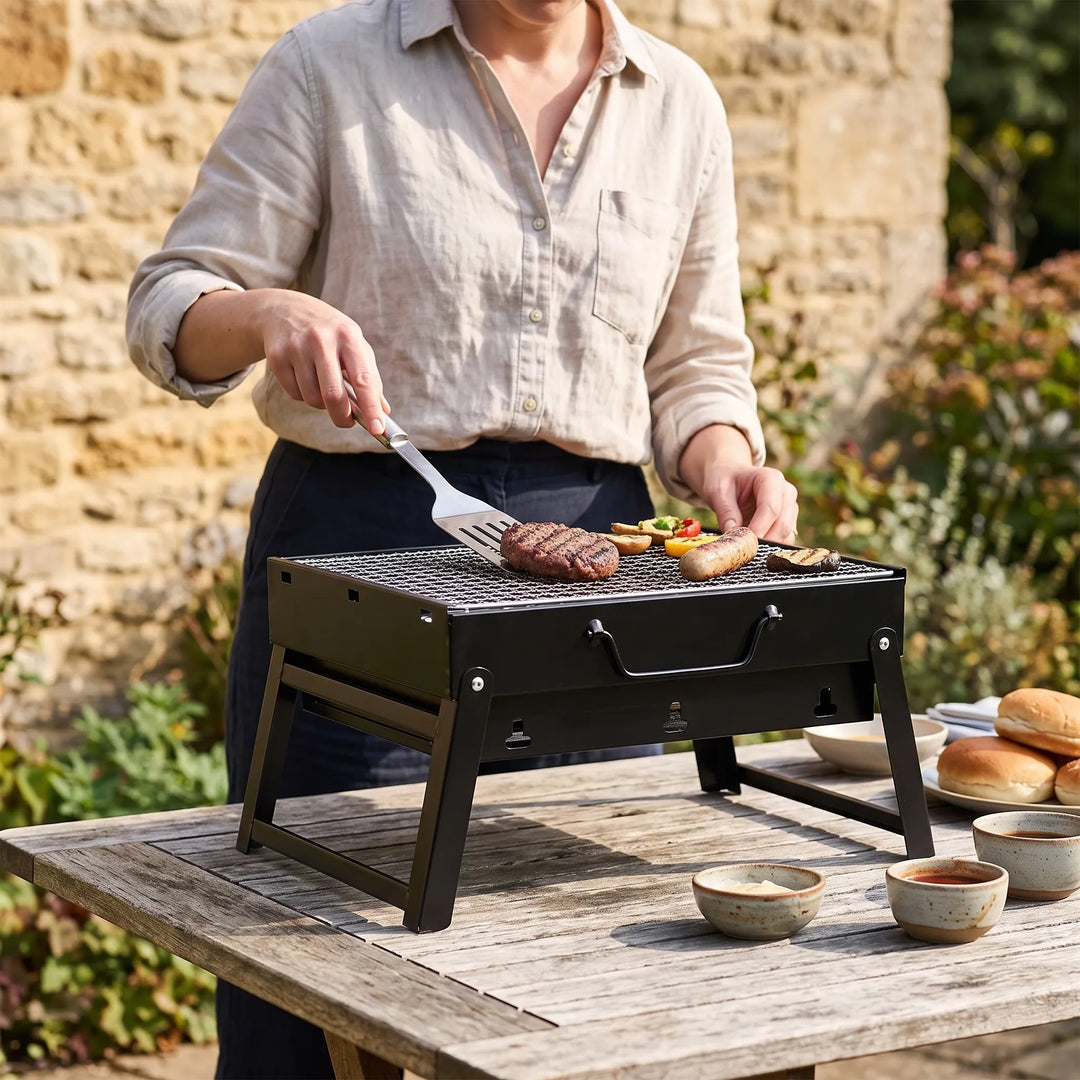 Portable folding charcoal grill for outdoor BBQ, camping, and picnics. Compact steel design.