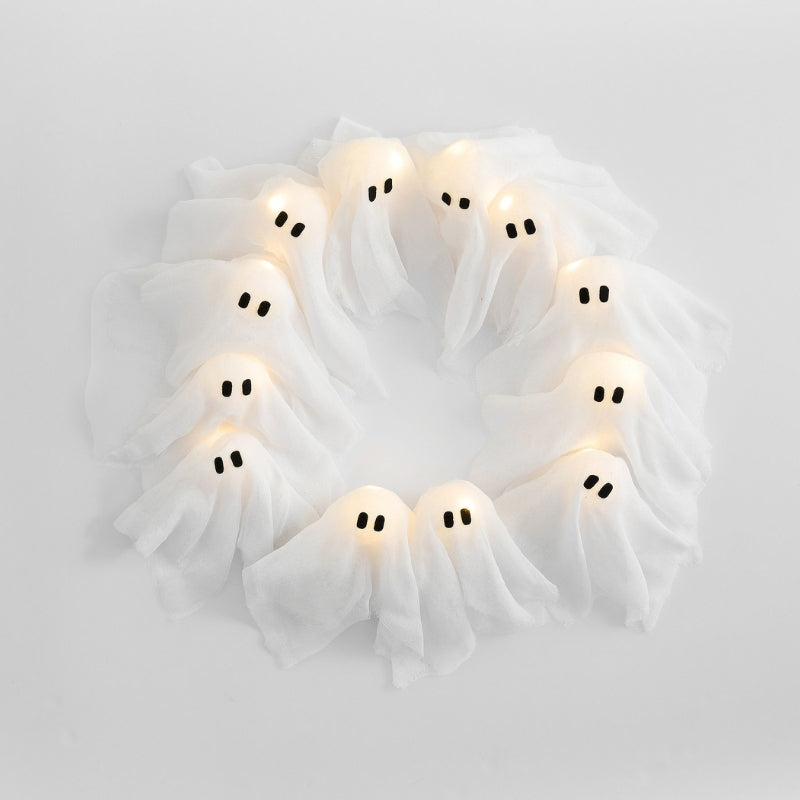 Close-up of a spooky Halloween wreath showing cute white fabric ghosts glowing with integrated LED lights on dark branches.