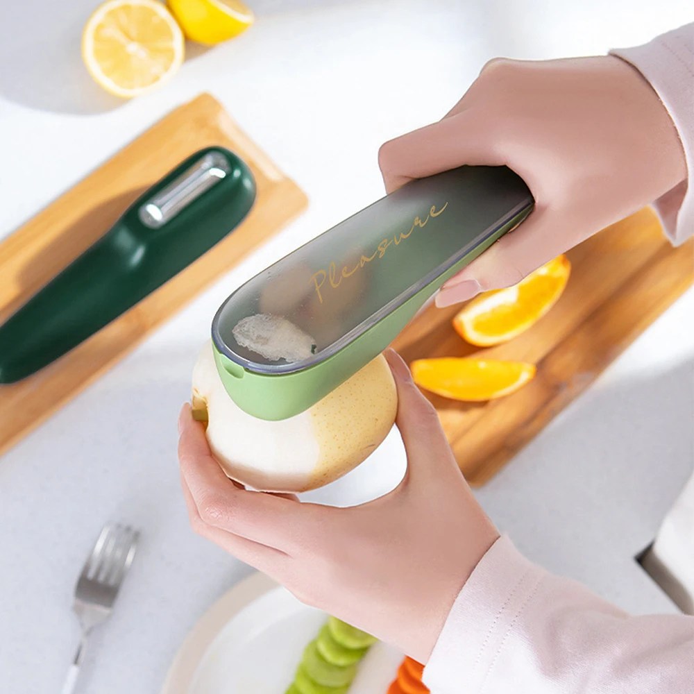 Close-up of the stainless steel vegetable peeler. Collects peels directly into its container for easy disposal.