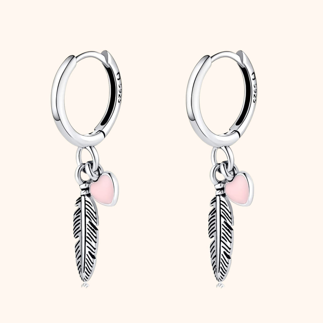 Sterling silver hoop earrings with delicate feather and heart charms. Elegant women's jewelry, perfect for everyday wear.