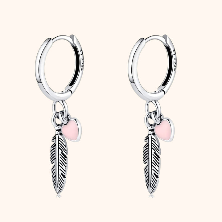 Sterling silver hoop earrings with delicate feather and heart charms. Elegant women's jewelry, perfect for everyday wear.