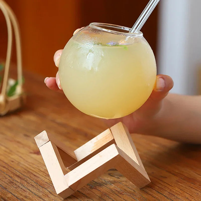 Hand-blown glass moon ball tumbler on a natural wooden base, enhancing any kitchenware or barware collection.