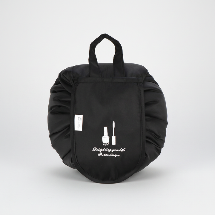 Unisex drawstring toiletry bag, GlamPouch, filled with beauty essentials, open and flat on a counter.