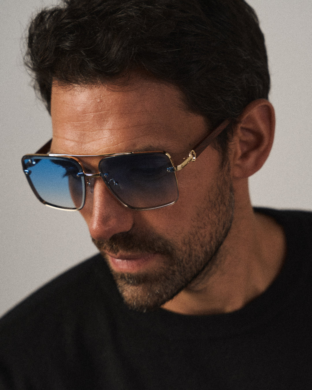 Close-up of modern classic unisex square sunglasses, showcasing natural woodgrain arms & gold frame.