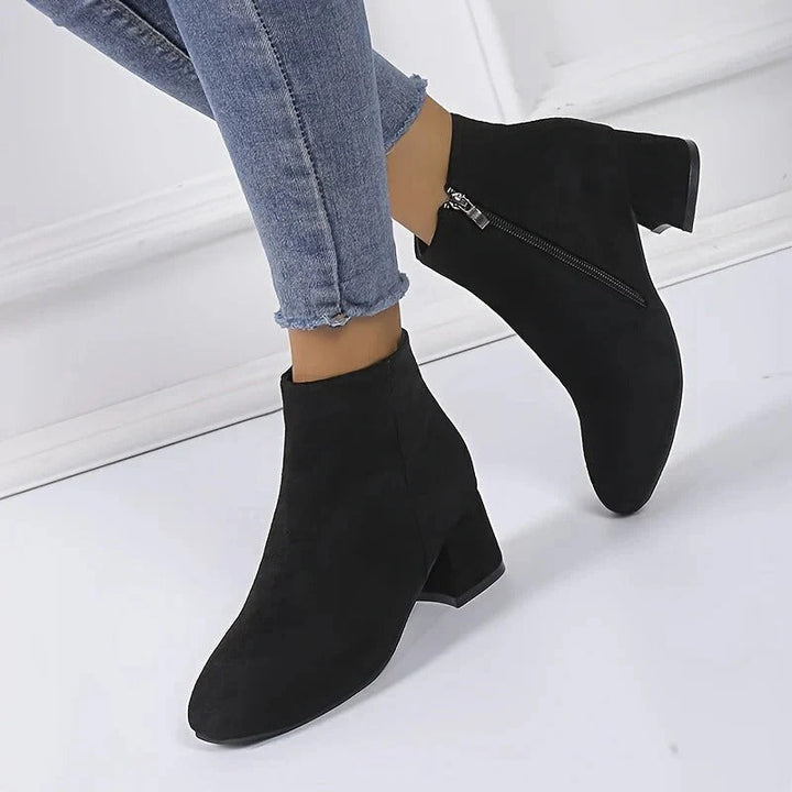 Sleek women's ankle boots, dark-colored, with a chunky block heel & easy-on side zip, great for casual outfits.