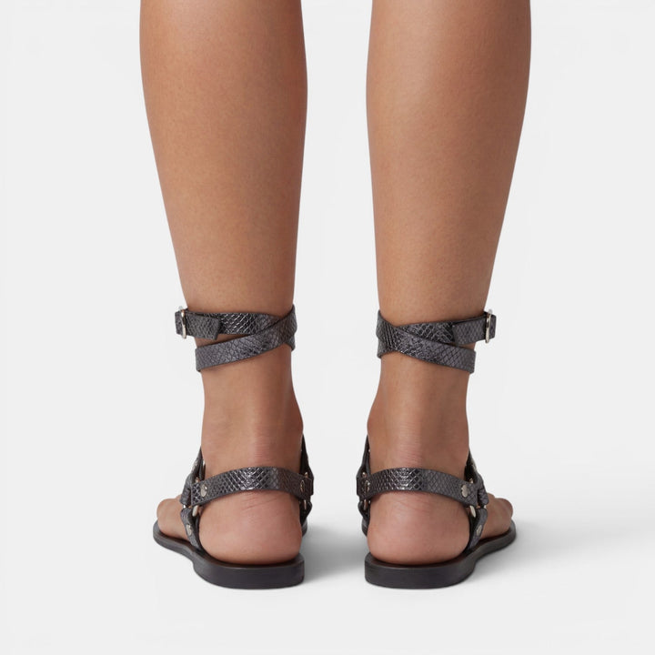 Women's stylish buckled flat sandals featuring a trendy snake print, crossover straps, and open toe design.