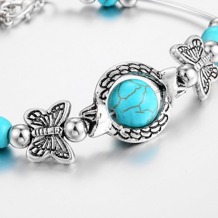 Women's wrist wearing an adjustable turquoise & silver butterfly beaded bracelet, elegant jewelry accessory.