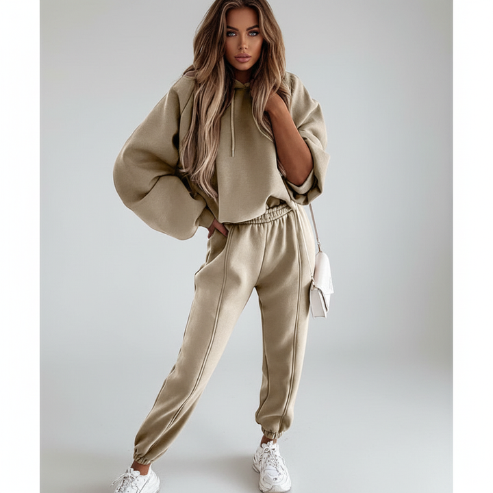 A woman smiling while relaxing in a 'Carla' women's hoodie and jogger set, emphasizing comfort