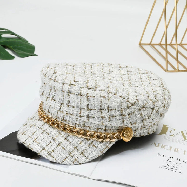 Close-up of a women's chic tweed cap with a prominent gold chain detail.