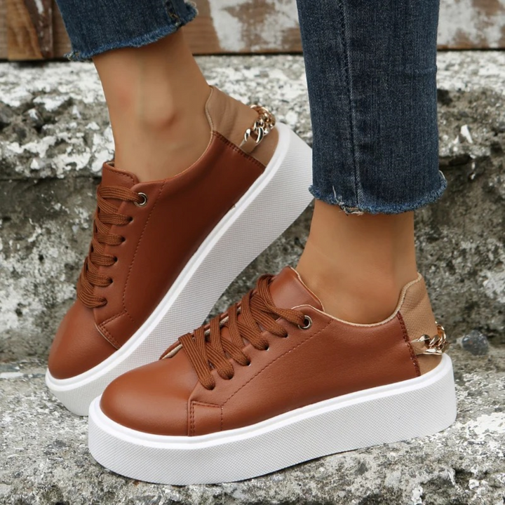 Women's chic white leather sneakers with elegant metal chain accent, perfect for casual everyday style & comfort.